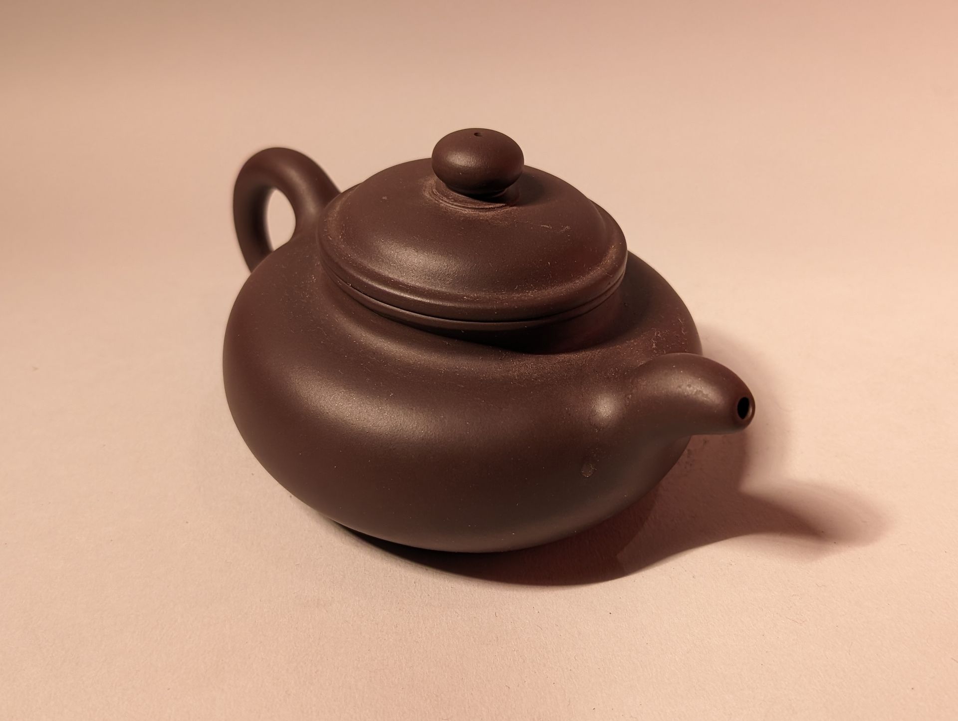 Brown ceramic teapot with lid on a light background, casting a shadow