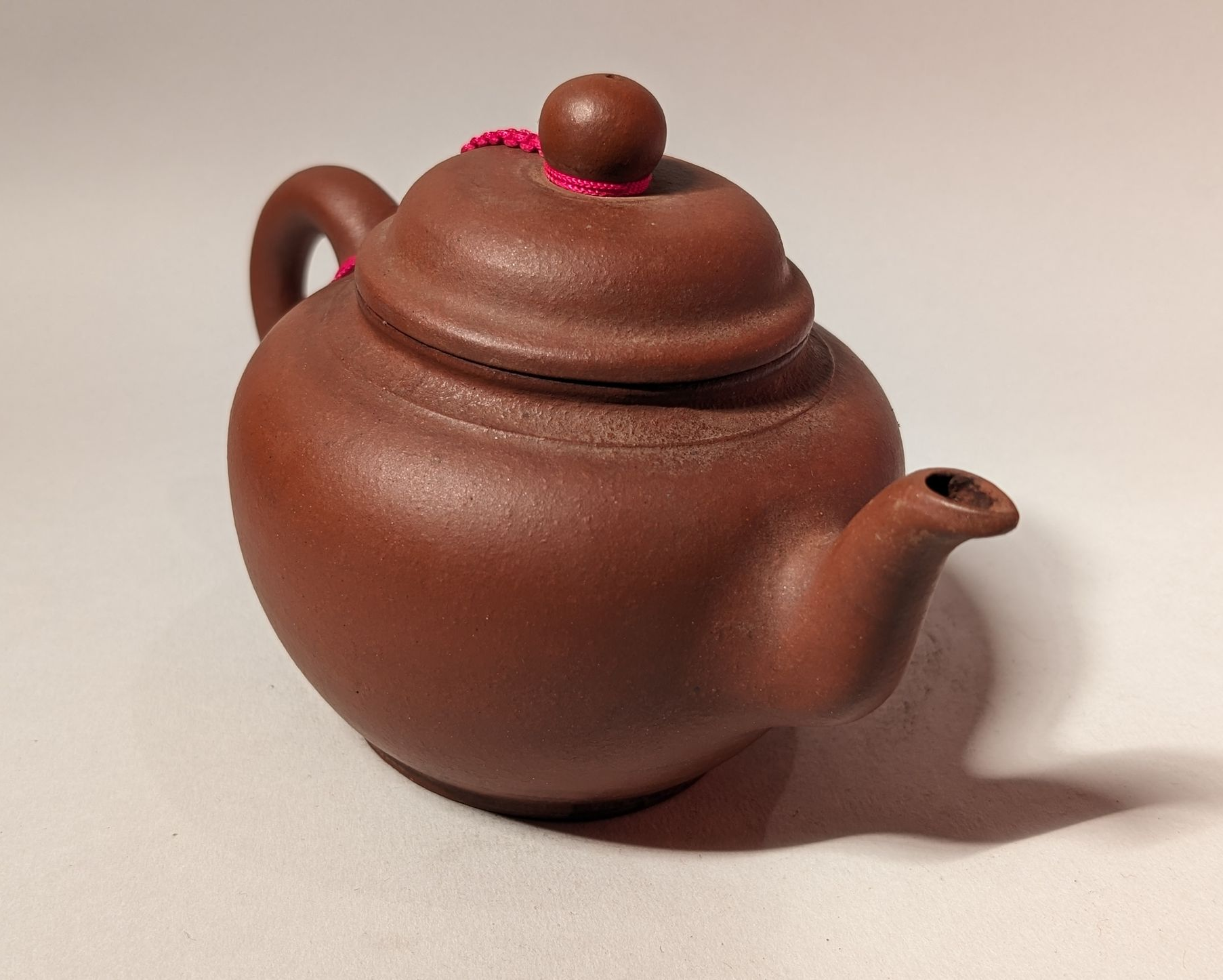 Small brown clay teapot with lid and curved spout on a light background