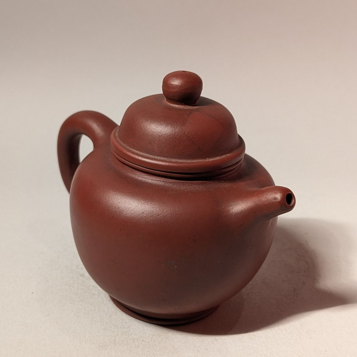 Small brown clay teapot with a lid and side handle on a plain background
