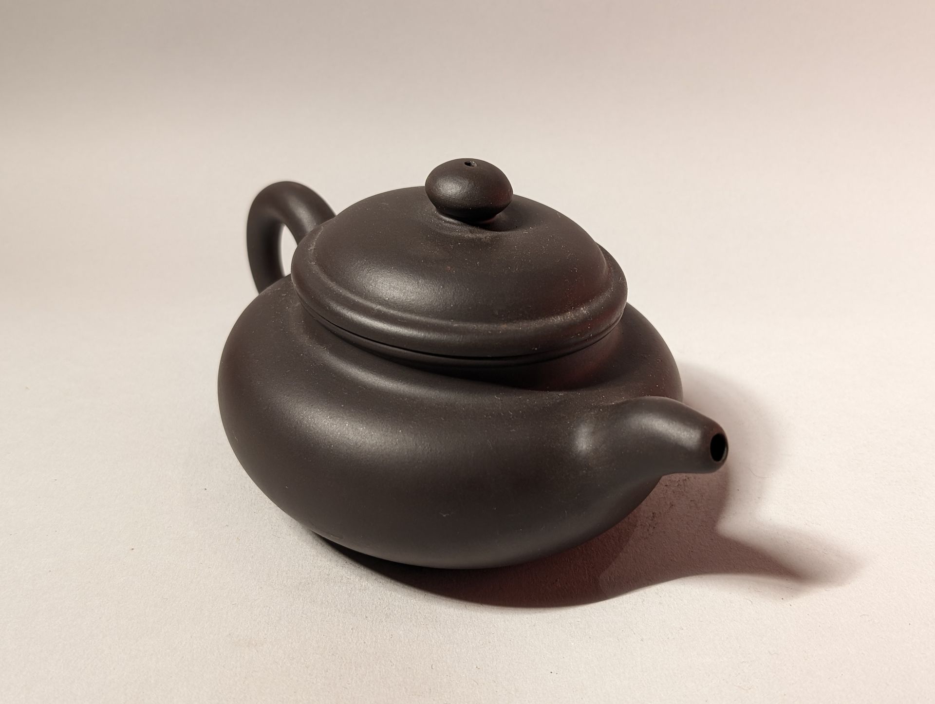 Dark brown teapot with lid and handle on a light background