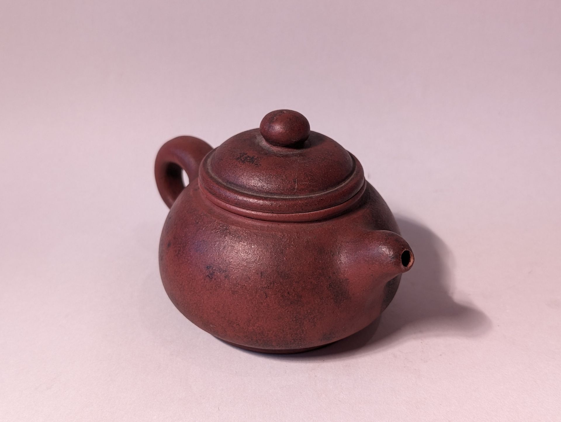 Small brown teapot with lid and handle on a plain light background