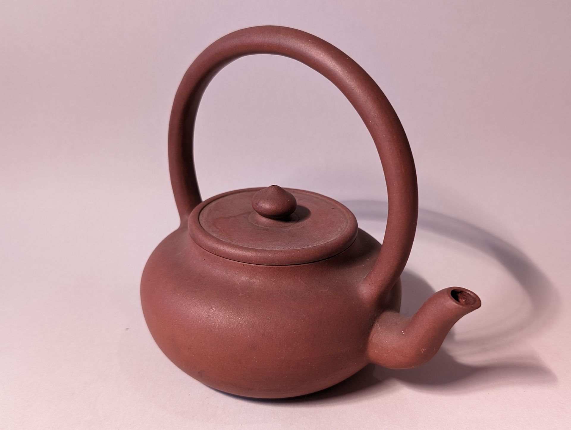 Brown ceramic teapot with a tall handle and short spout on a light background