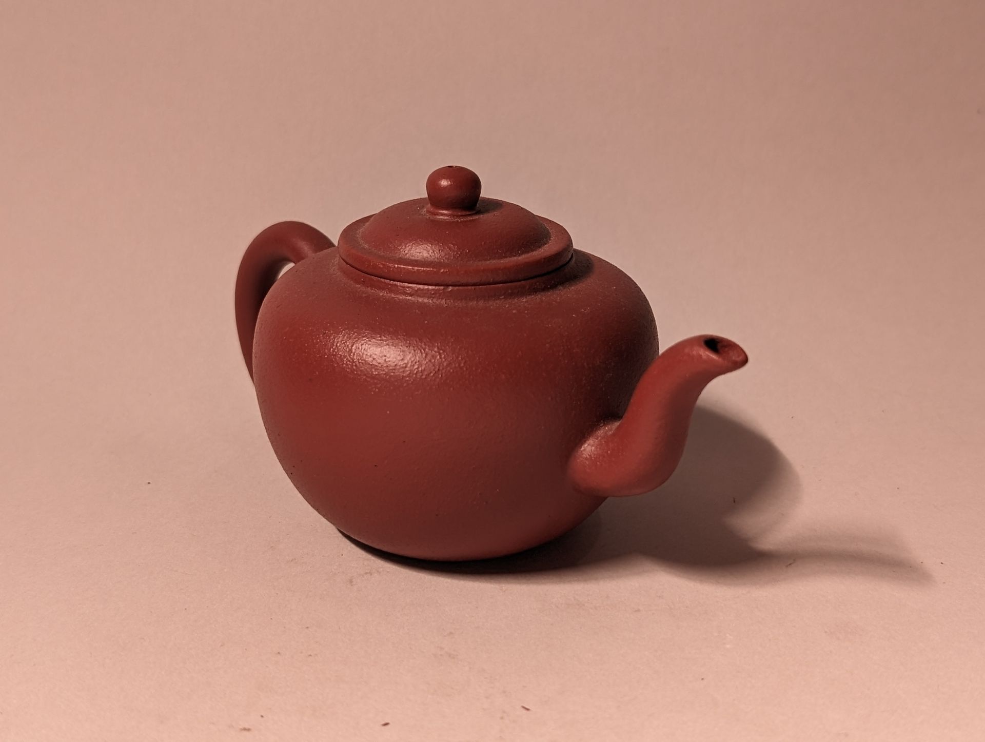 Small red ceramic teapot with a lid, shown on a plain light background.