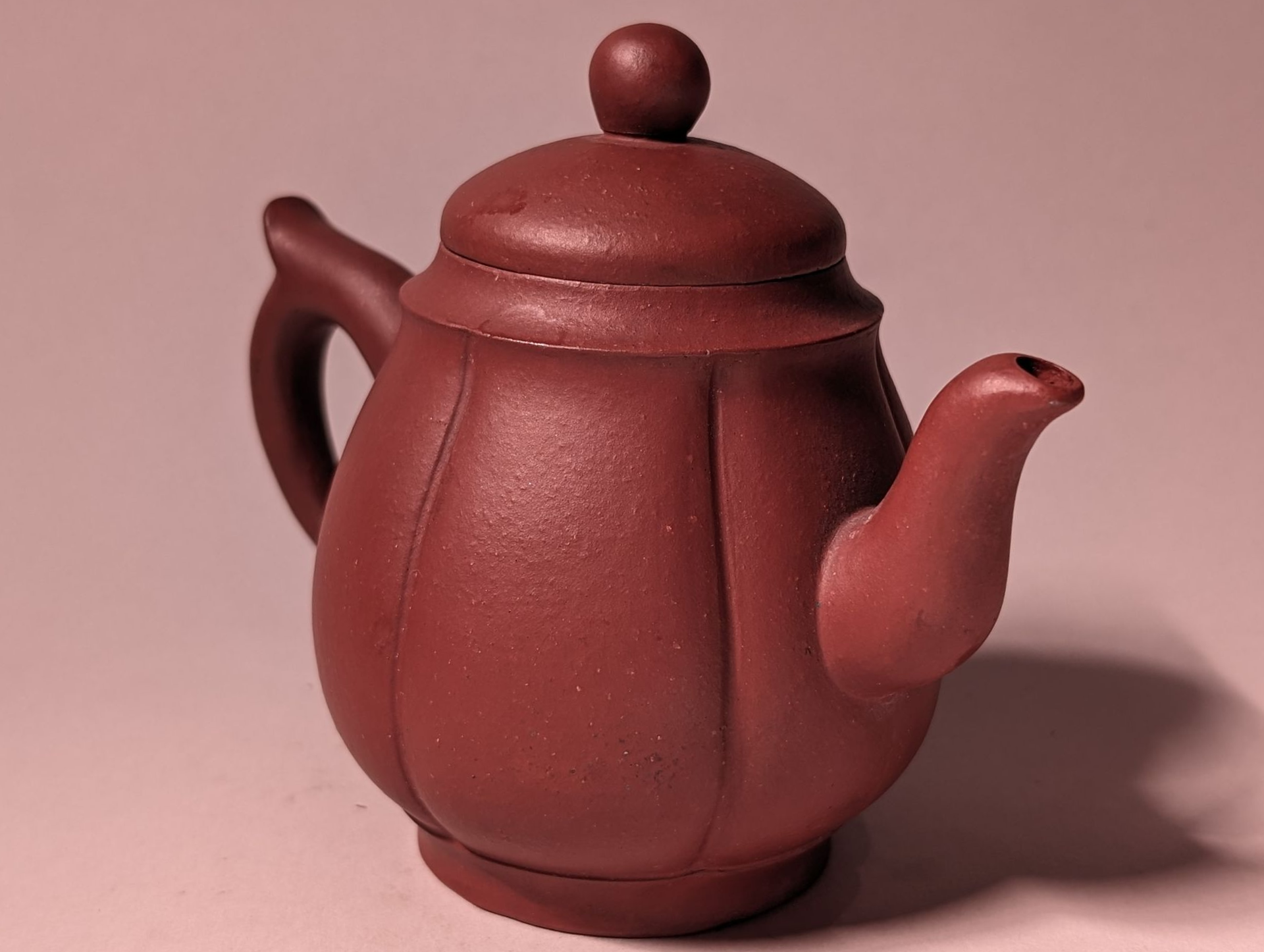 Red ceramic teapot with a round lid and curved spout on a pink background