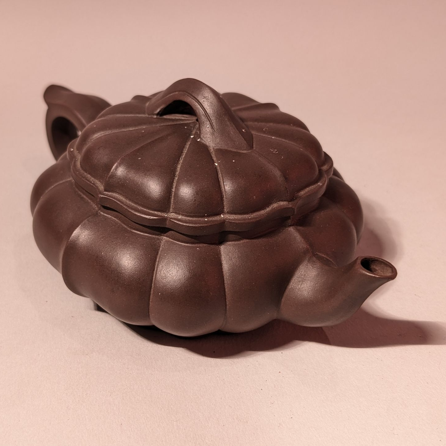 Dark brown ceramic teapot with a rounded, ribbed body and lid on a beige surface.