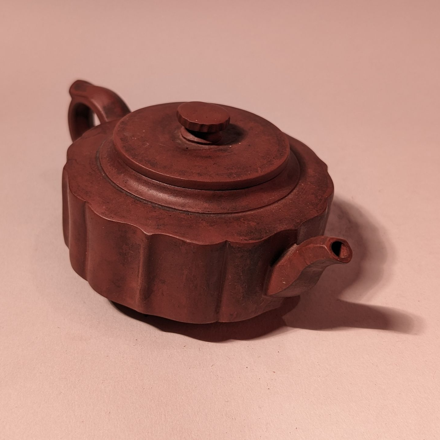 Small brown ribbed ceramic teapot with a lid on a plain background