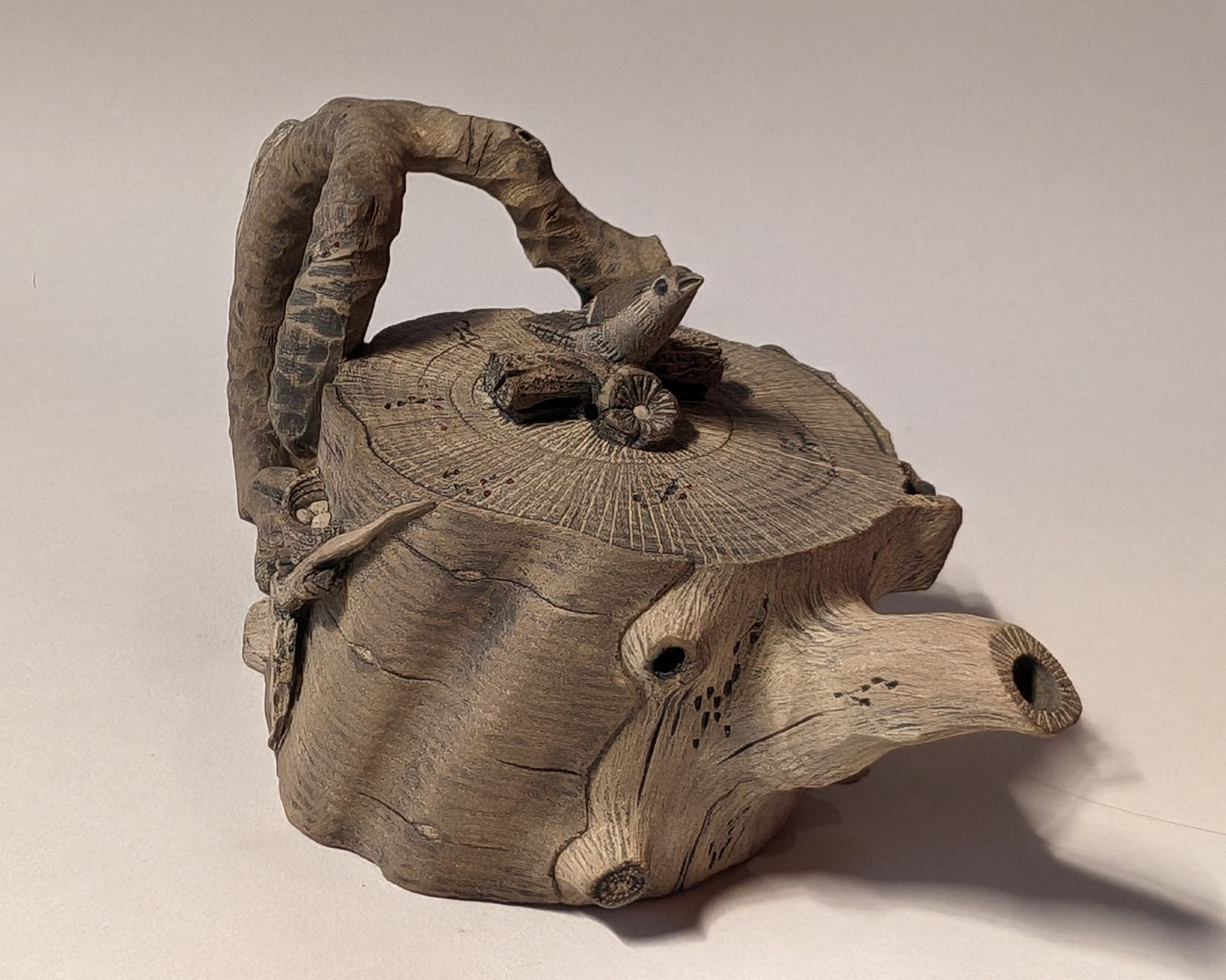 Rough clay teapot with a twisted handle and round lid on a plain light background