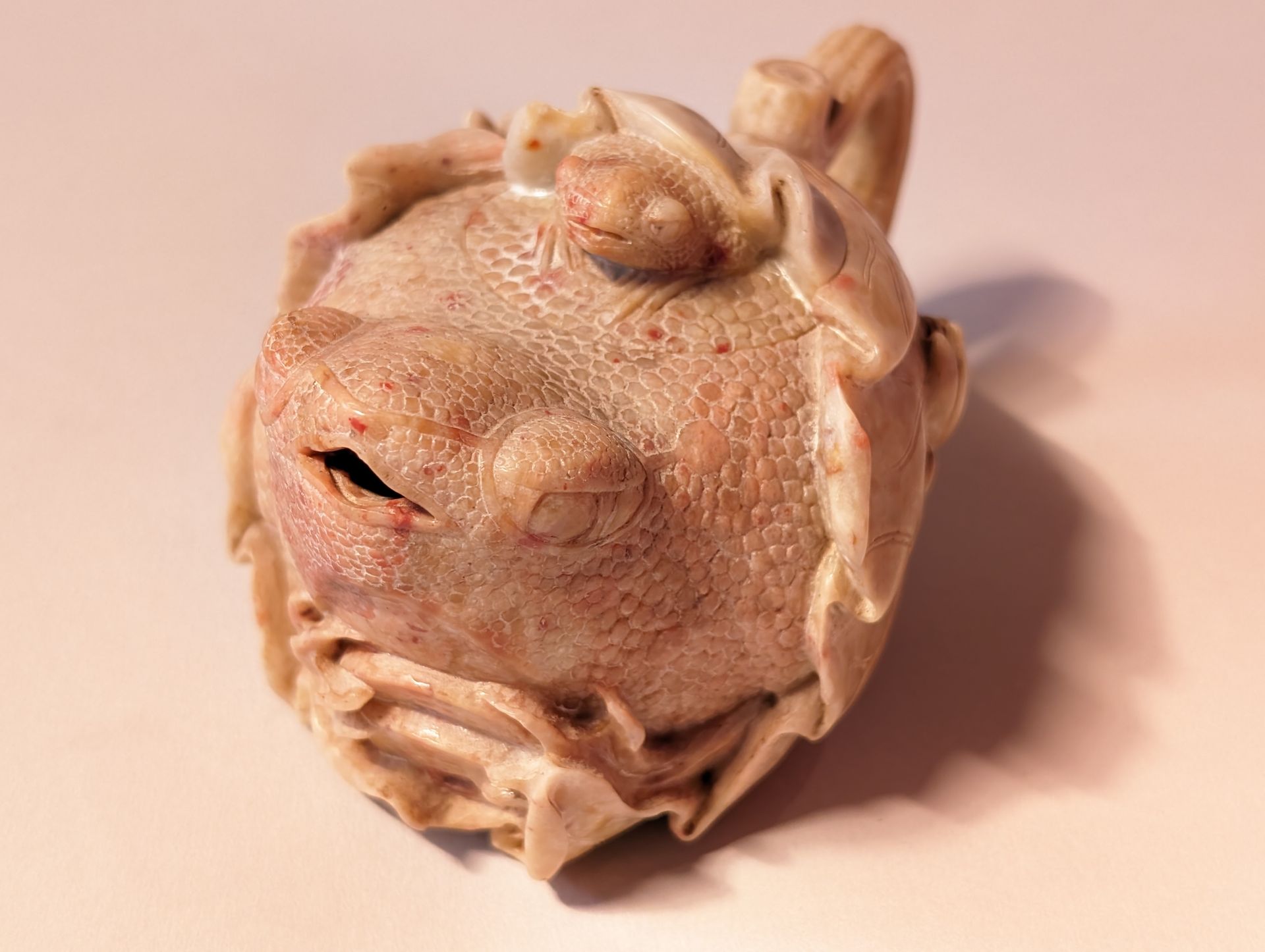 Small beige clay figurine with a round face and curled details, resting on a light pink surface.