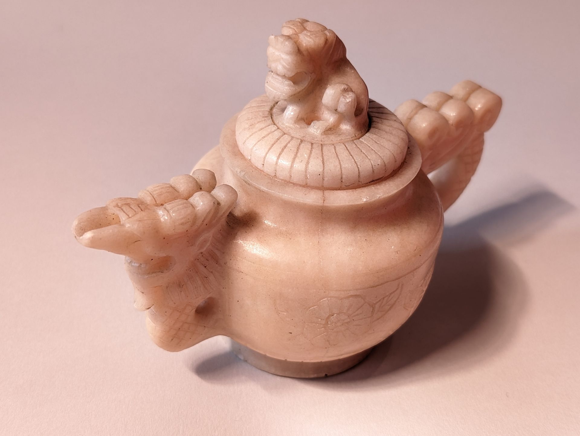 Small carved wooden teapot with a round lid and decorative bird-like handles on a pink background