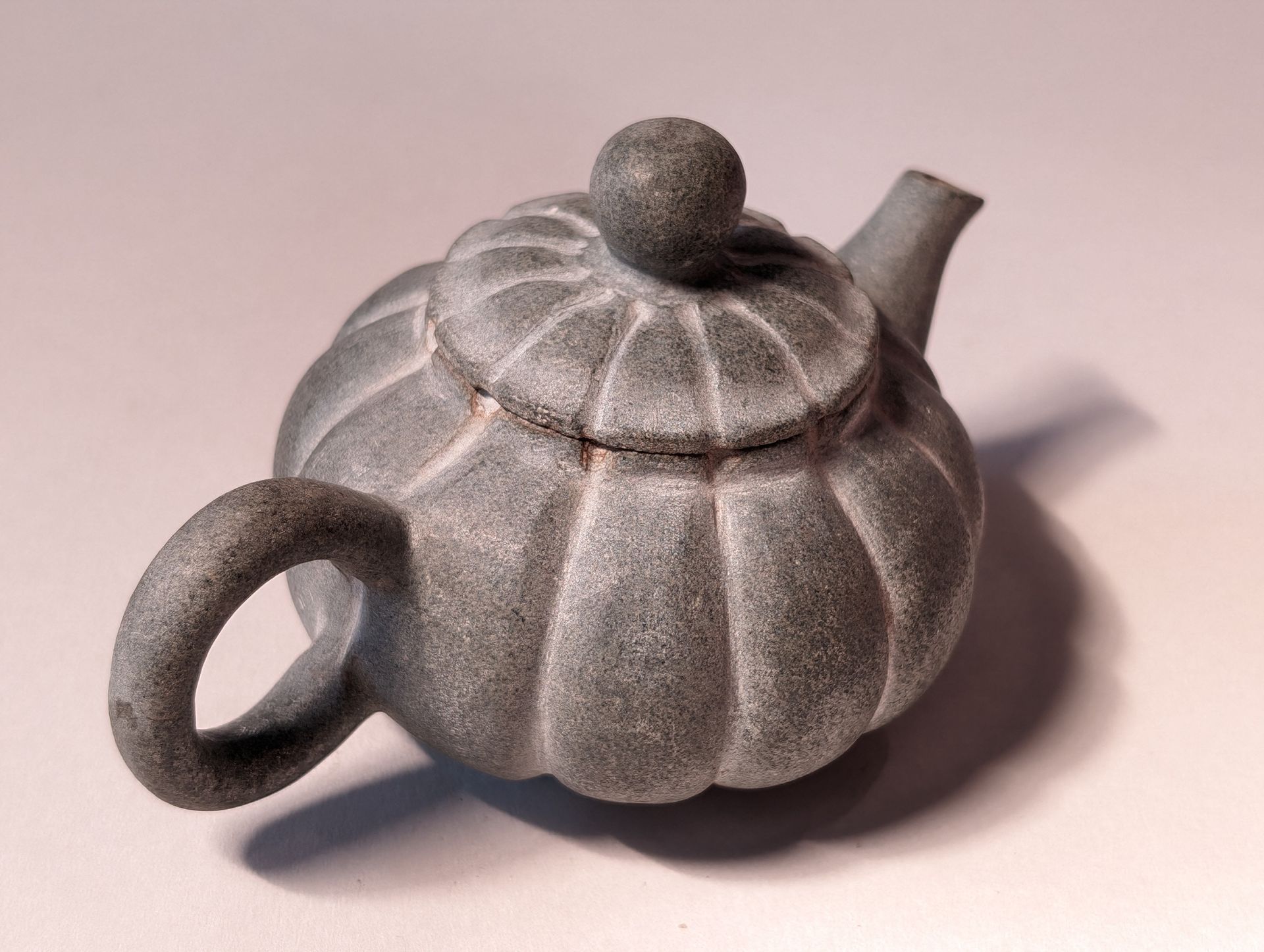 Small gray ceramic teapot with a loop handle and rounded lid on a light background