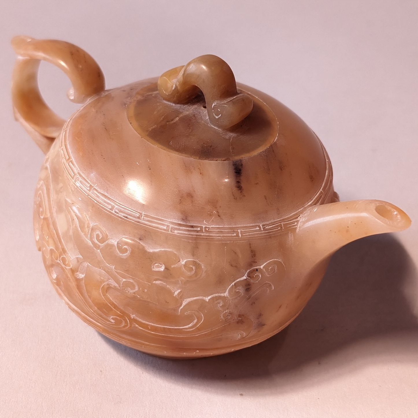Decorative tan ceramic teapot with carved floral pattern and curved spout and handle