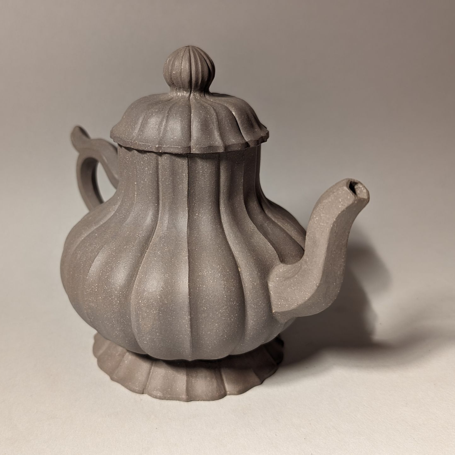 Gray ribbed teapot with a lid and curved spout, displayed on a plain background