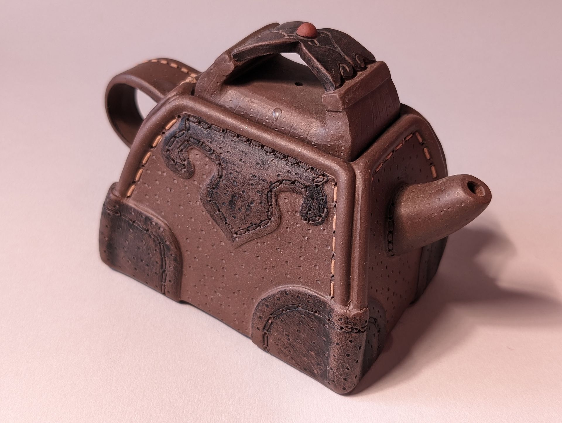Brown ceramic teapot with ornate raised design and handle on a light background