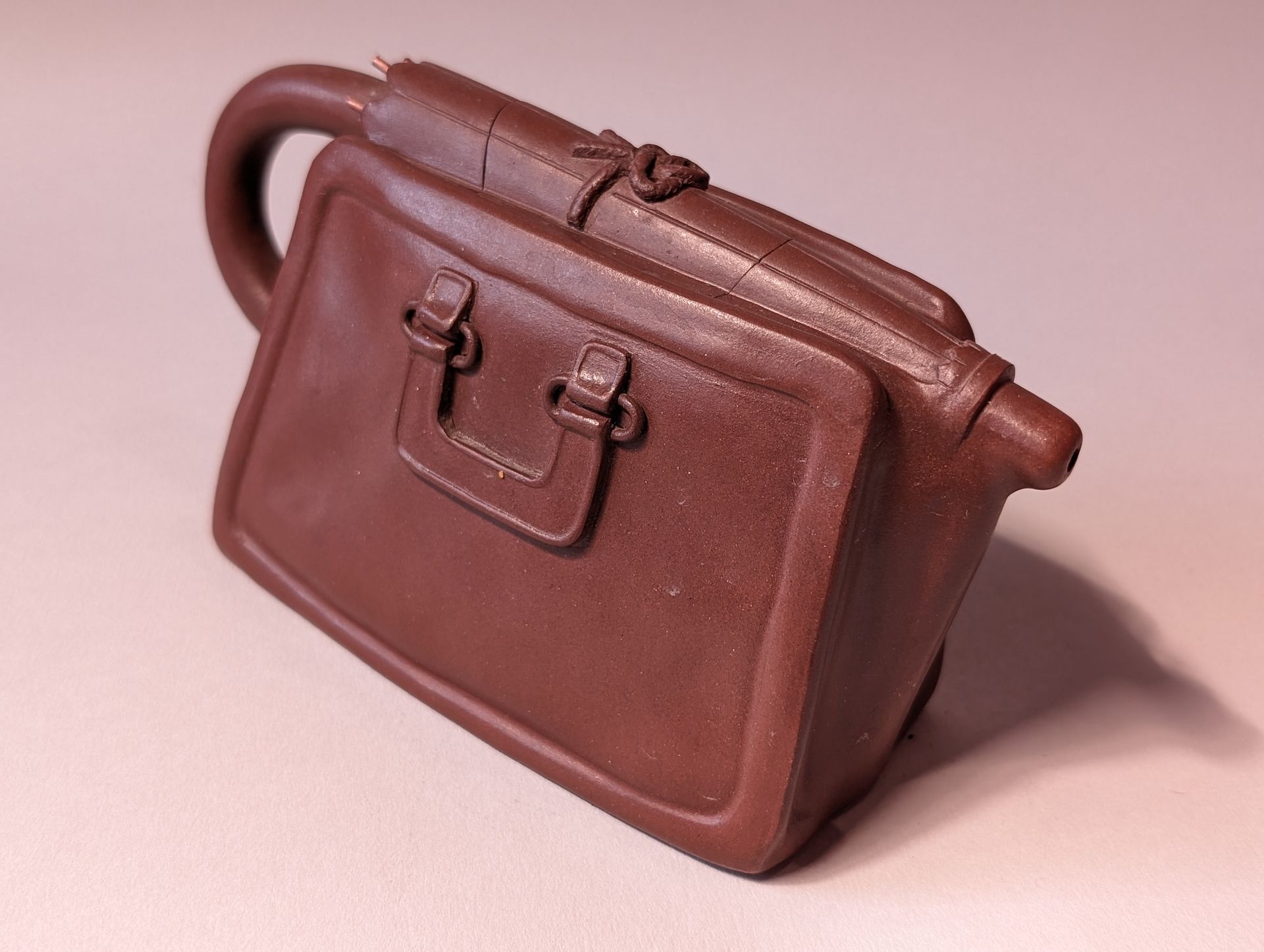 Brown leather handbag on a pink surface, shown from the side with a top handle and clasp closure