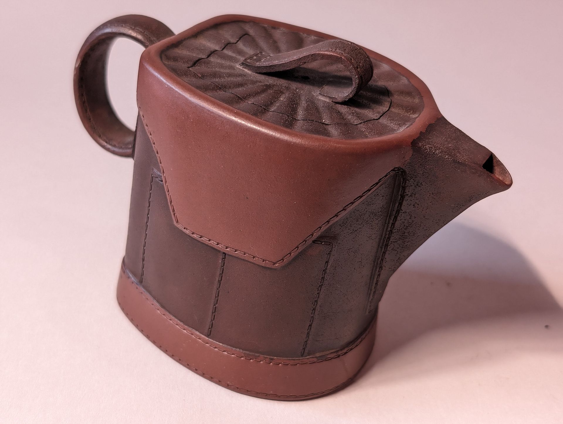 Brown ceramic teapot with a curved handle and spout, viewed on a white background