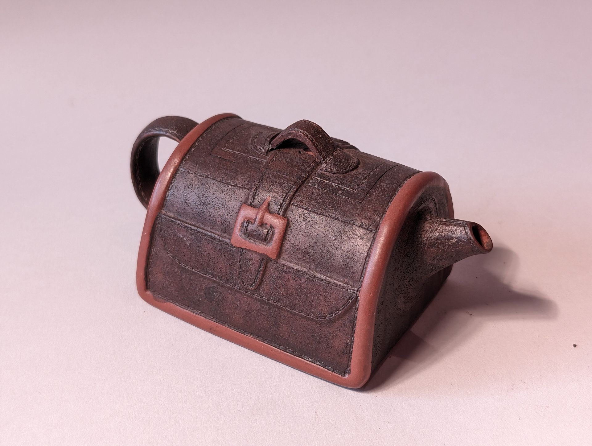 Small brown leather pouch with a flap, strap, and curved handle on a light background