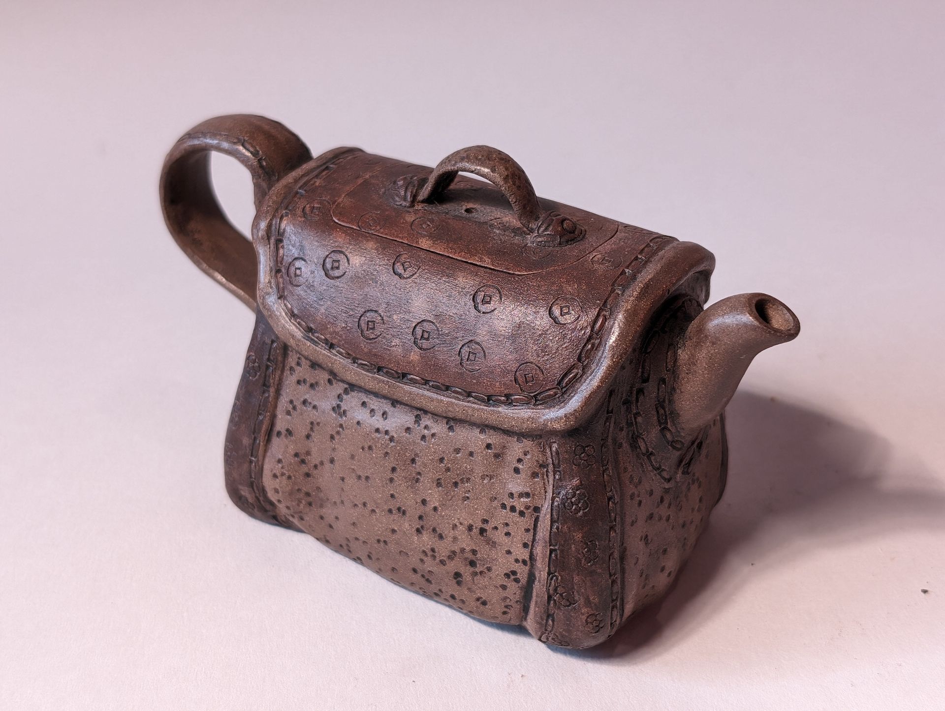 Small brown ceramic teapot with a curved handle and lid on a plain background