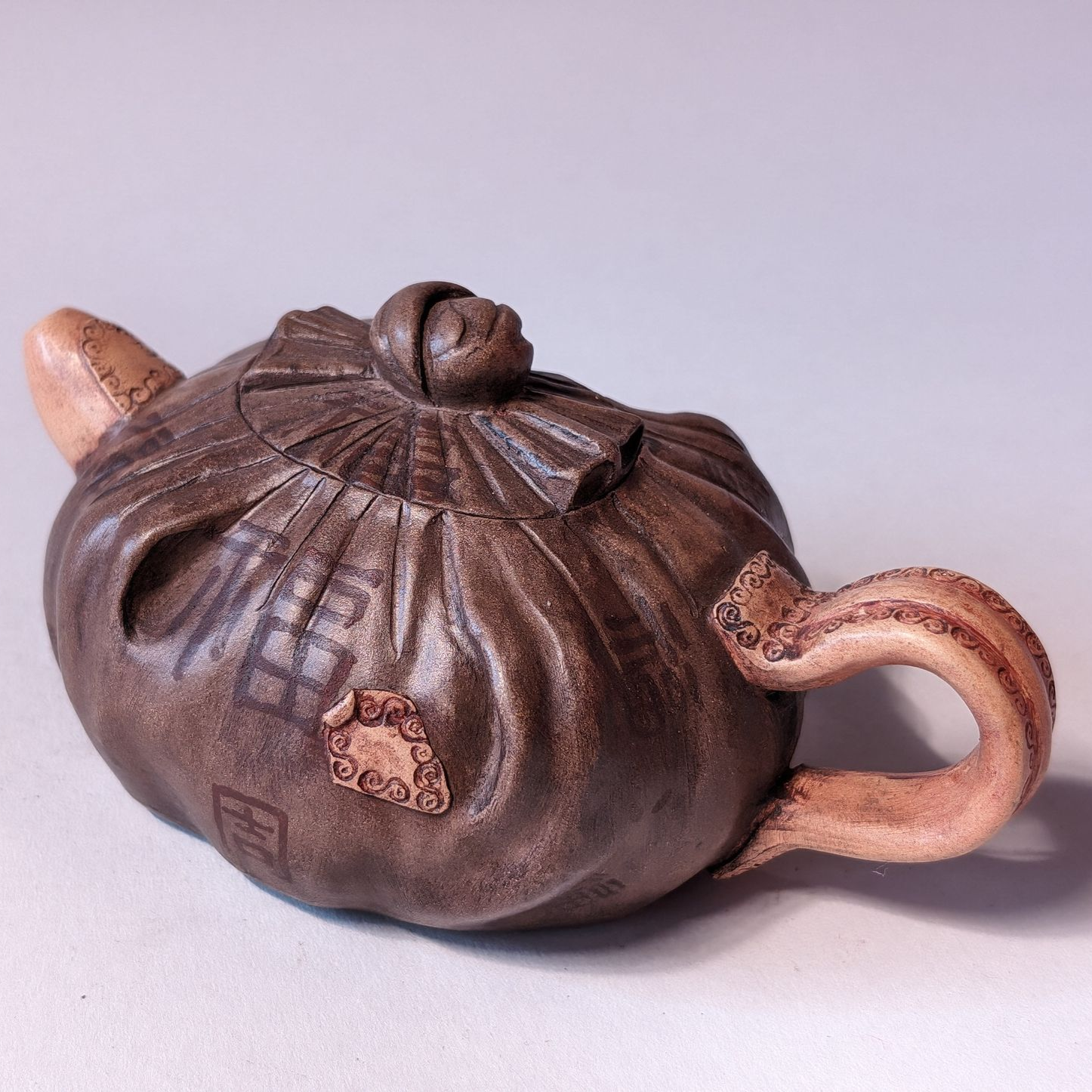 Brown ceramic teapot with textured lid and curved handle on a light background