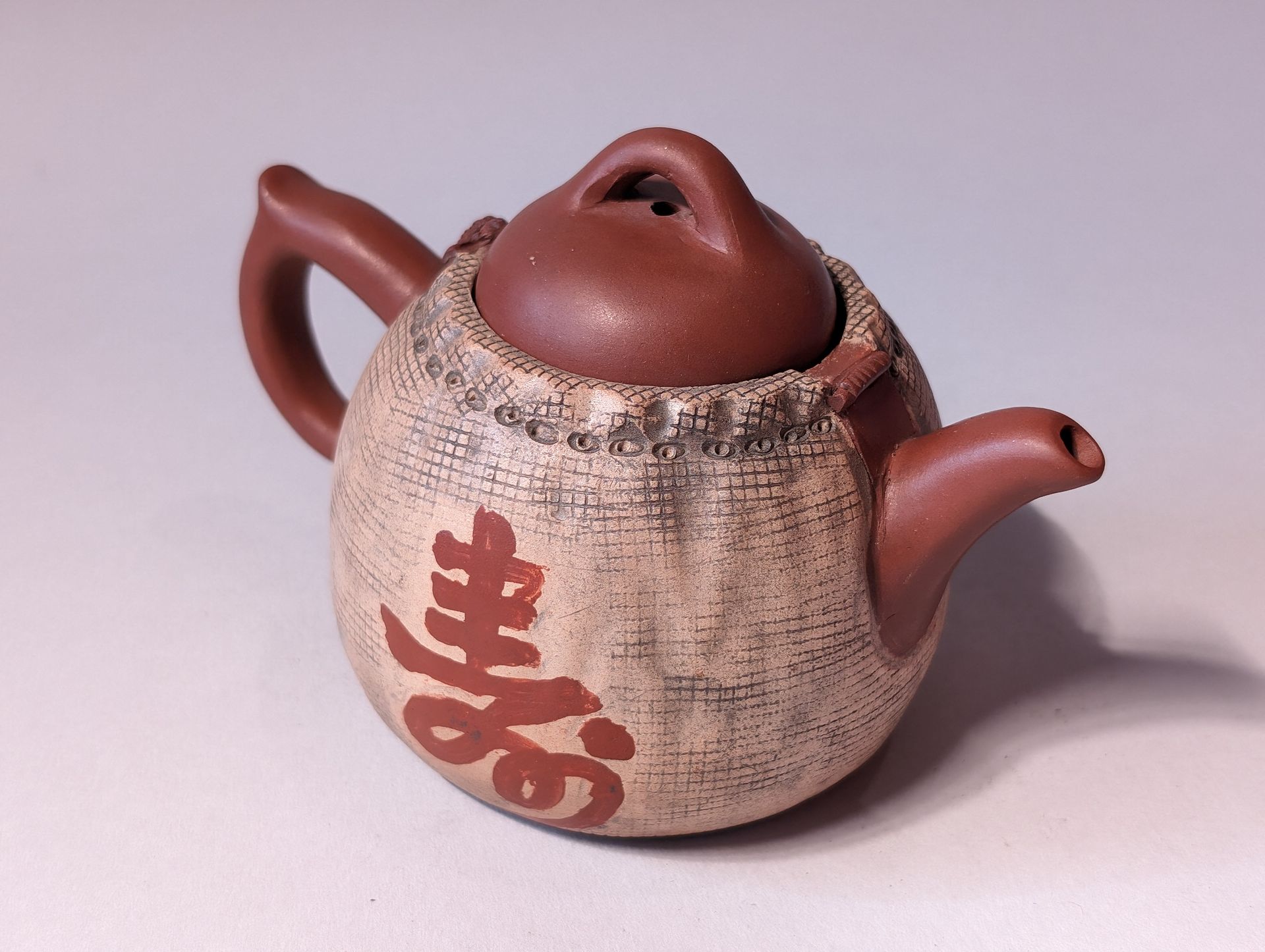 Brown ceramic teapot with textured beige body and red Japanese characters, on a plain background