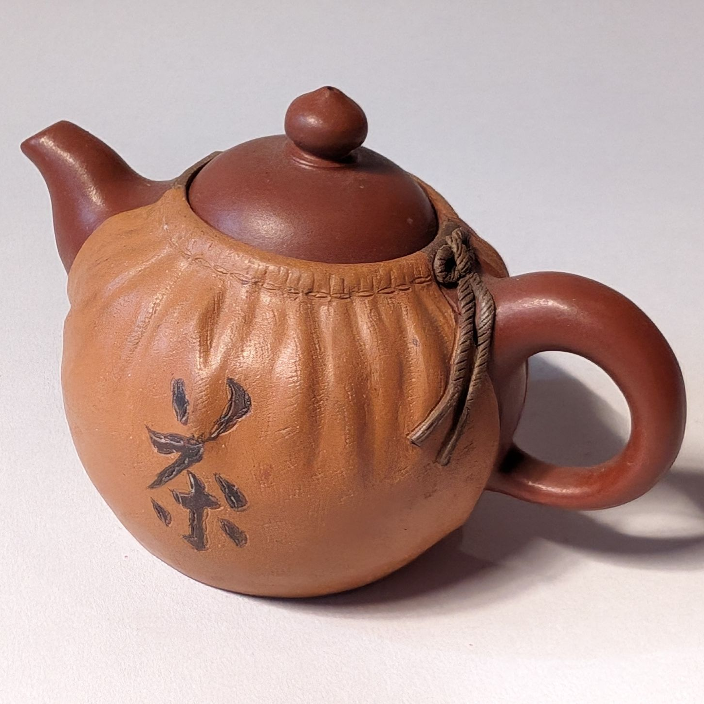 Small brown clay teapot with lid, curved handle, and black character marking