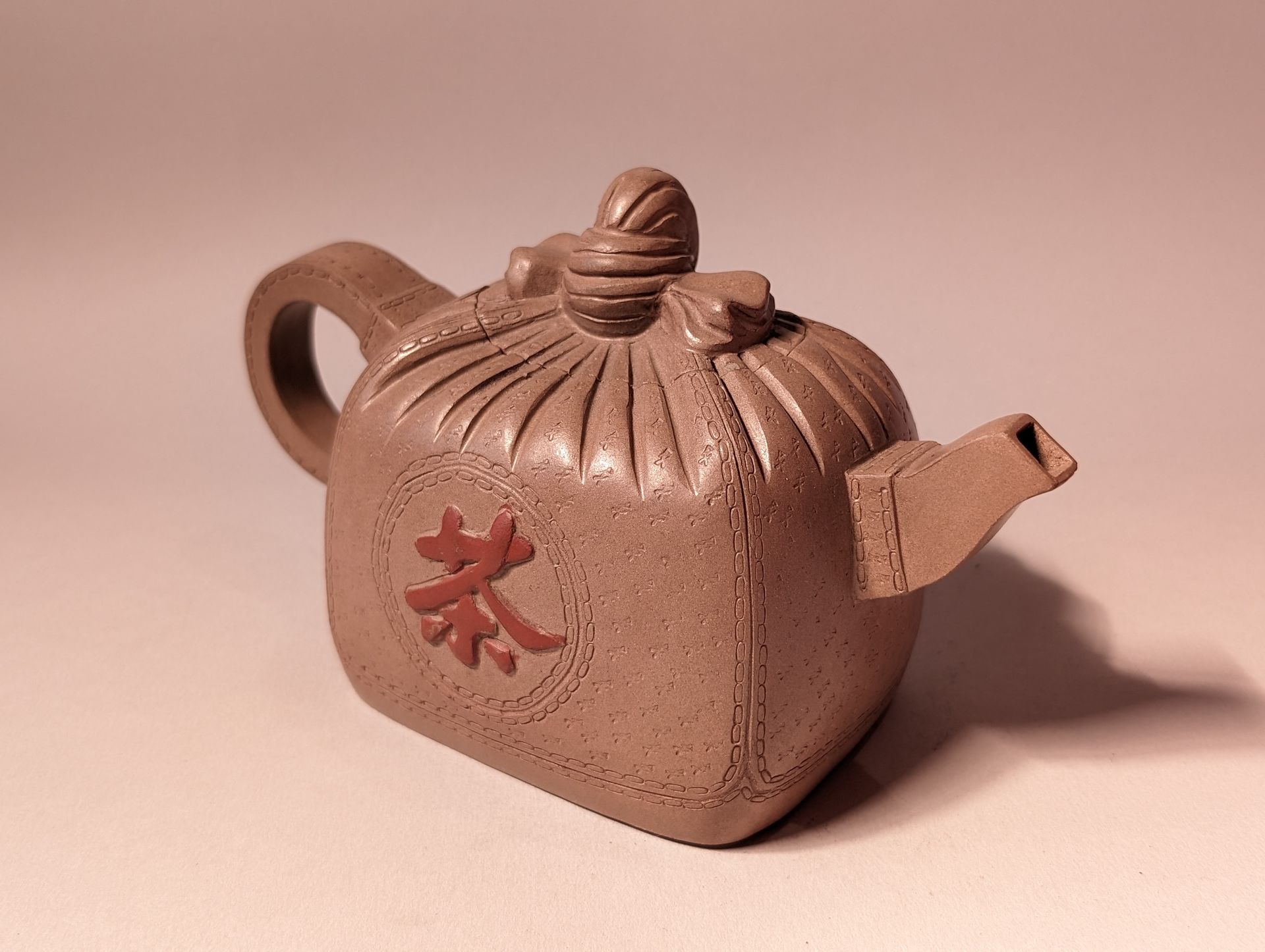 Small brown ceramic teapot with a red Chinese character on a plain background