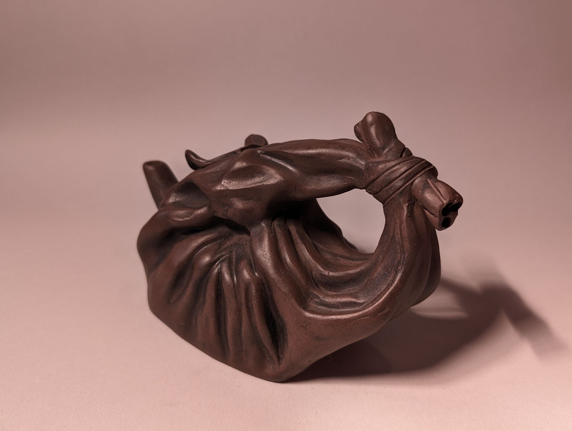 Small brown carved figurine of a curled figure with arms crossed over a light background