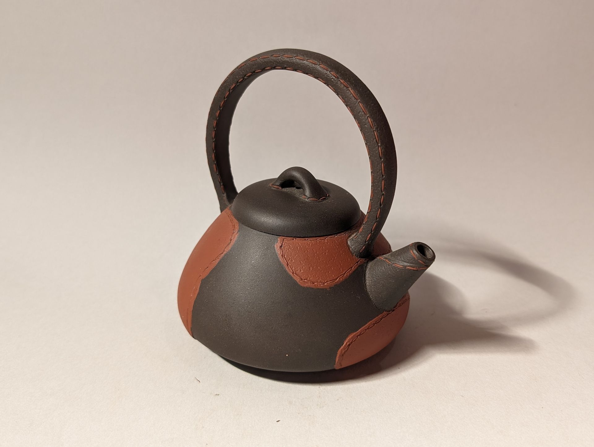 Small black-and-red teapot with a curved handle on a white background