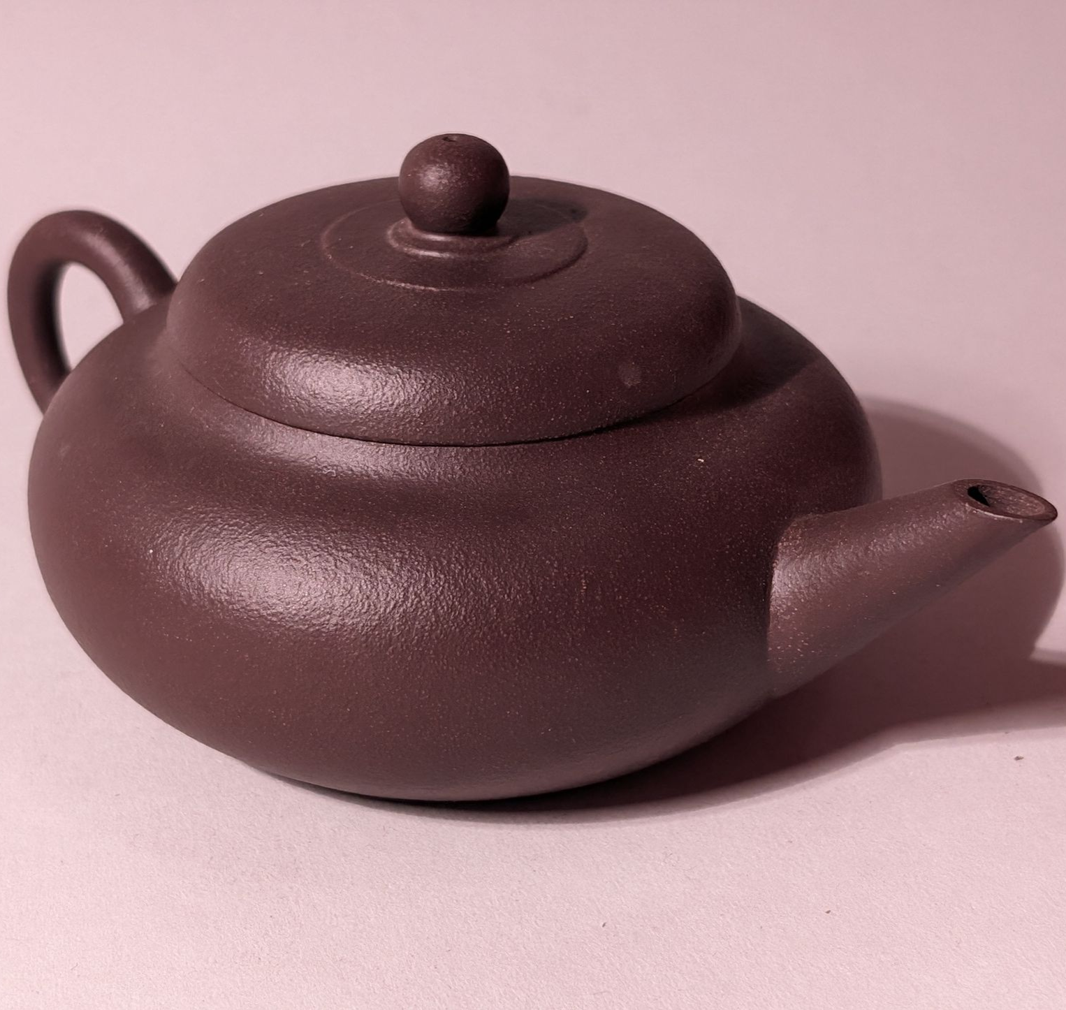 Purple ceramic teapot with lid and curved spout on a pink surface