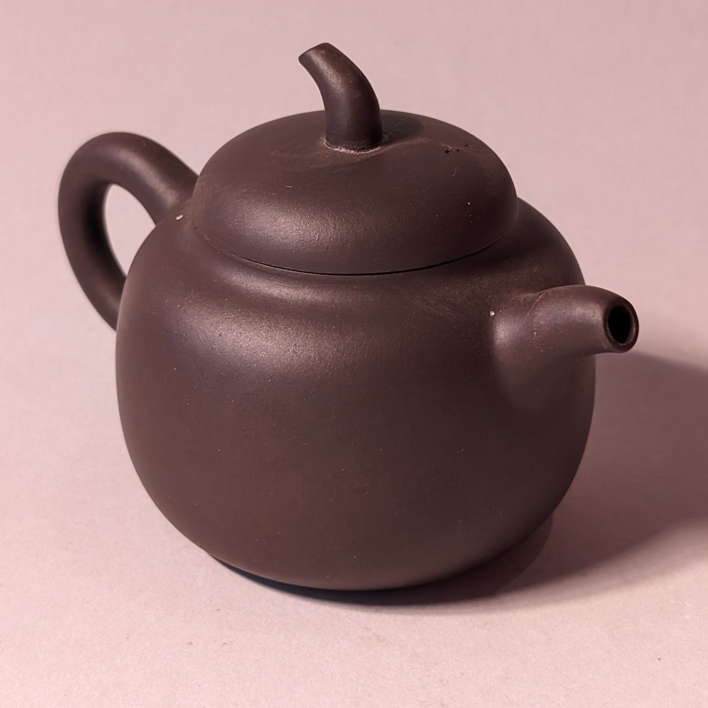 Dark brown ceramic teapot with a curved handle and spout on a pink surface