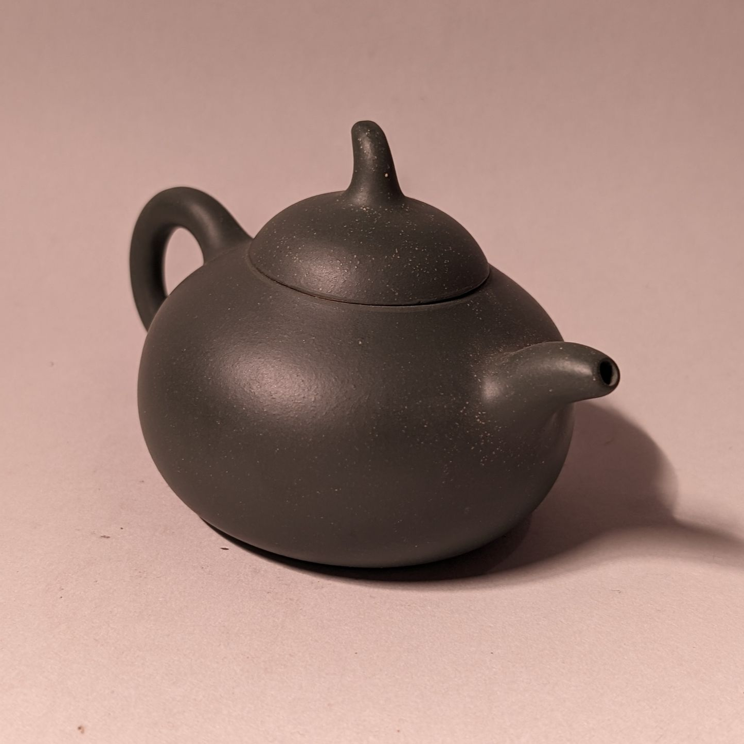 Dark gray teapot with a curved handle and short spout on a pink surface