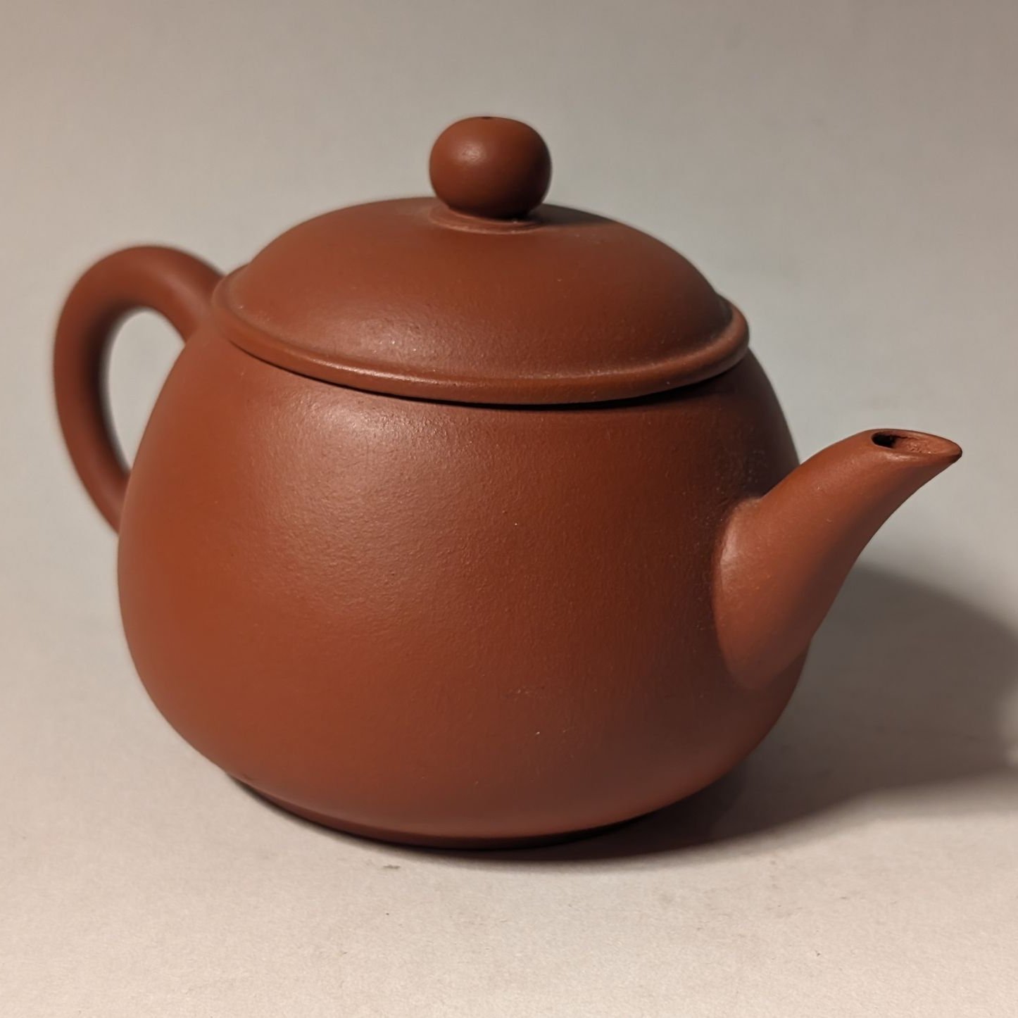 Brown clay teapot with lid and rounded handle on a plain background