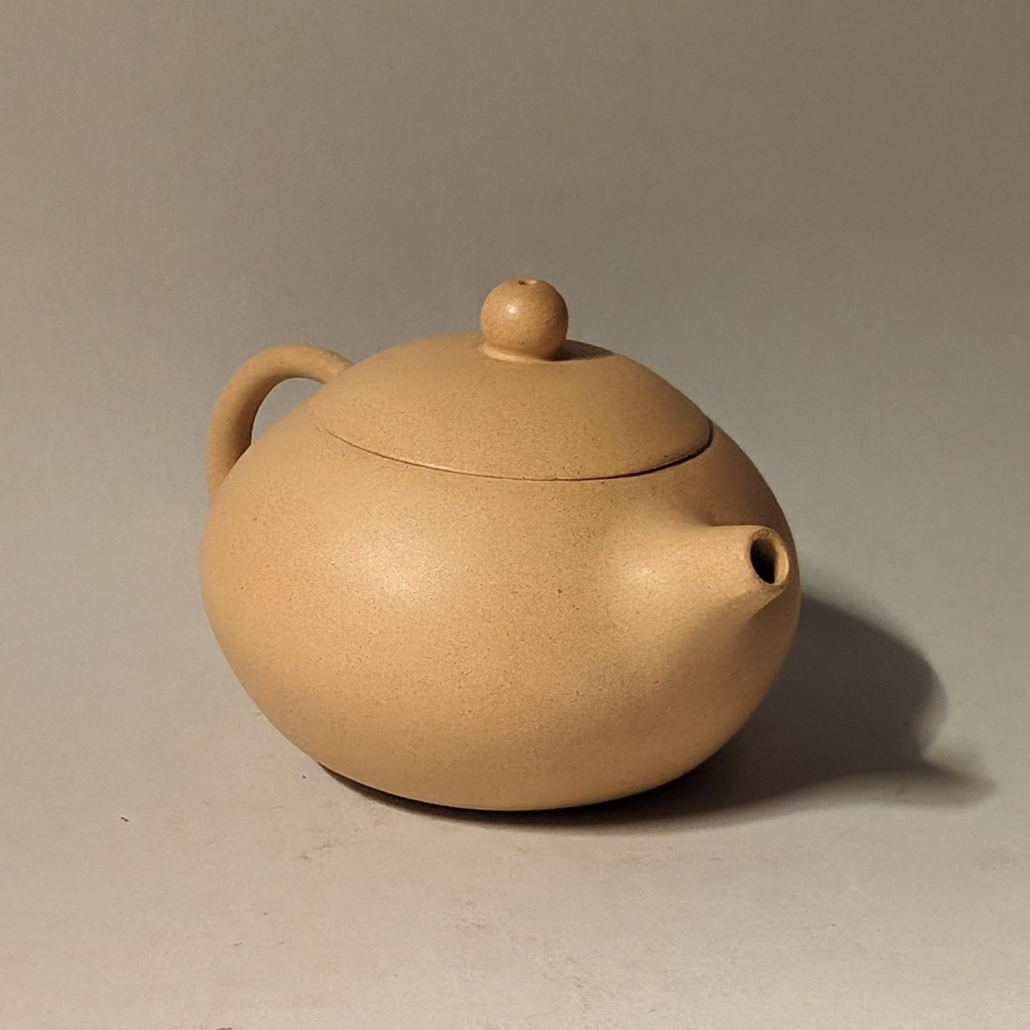 Beige ceramic teapot with a rounded body and small lid on a plain background