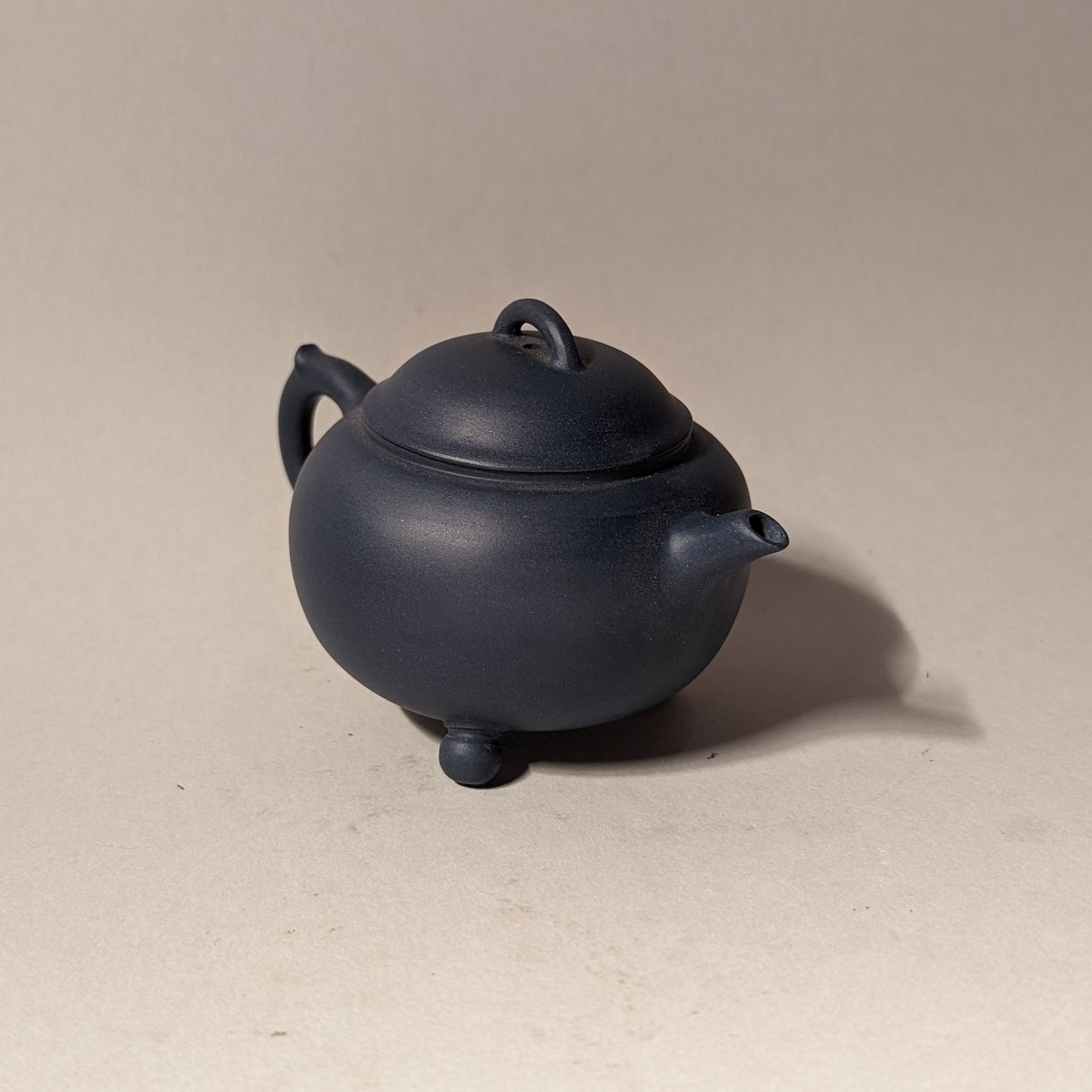 Small dark blue teapot-shaped ceramic object on a beige surface.