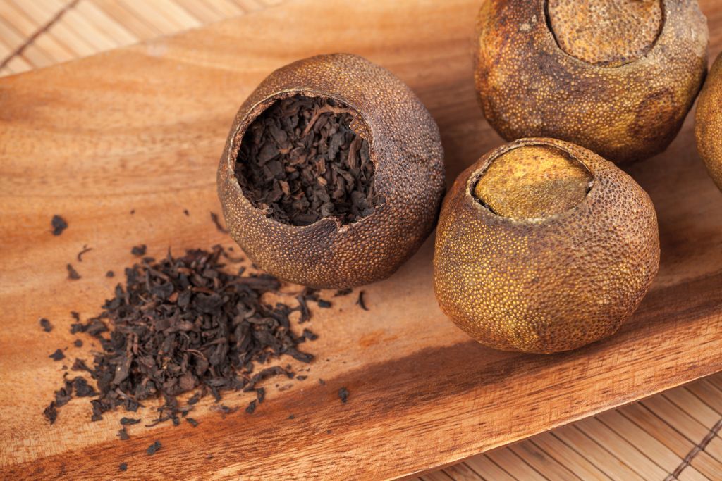 Dried black tea leaves spilled beside round tea balls on a wooden tray