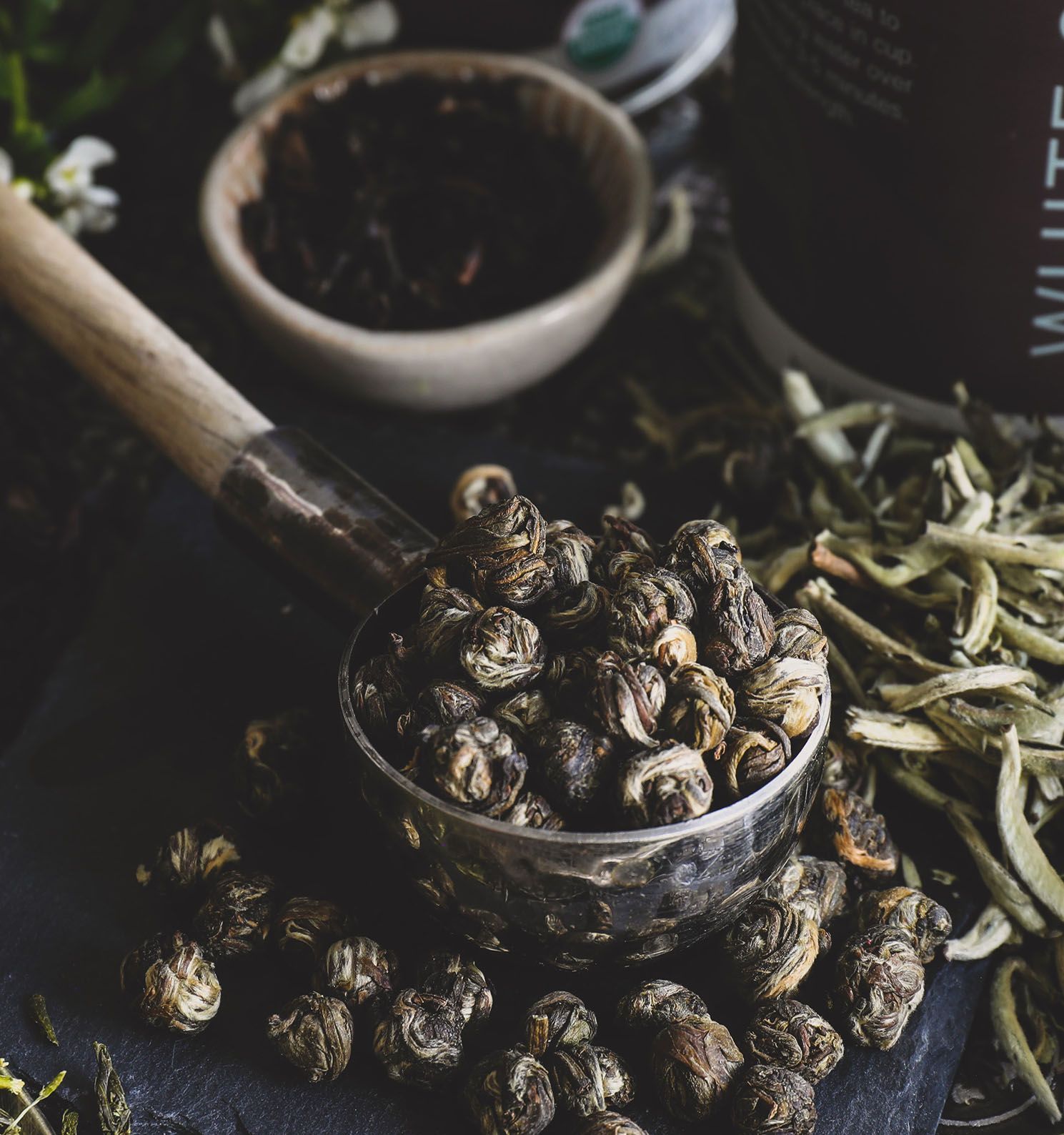 Scoop of dried spices in a small bowl with scattered herbs on a dark tabletop