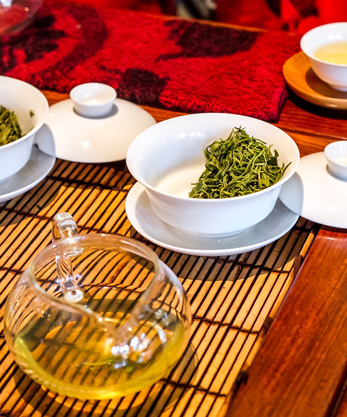 Tea set with glass teapot and white bowls of green tea on a bamboo mat
