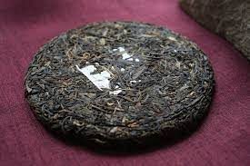 Round compressed tea cake on a burgundy cloth, wrapped in clear plastic.