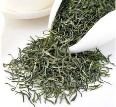 Loose green tea leaves spilling from a white scoop onto a white surface