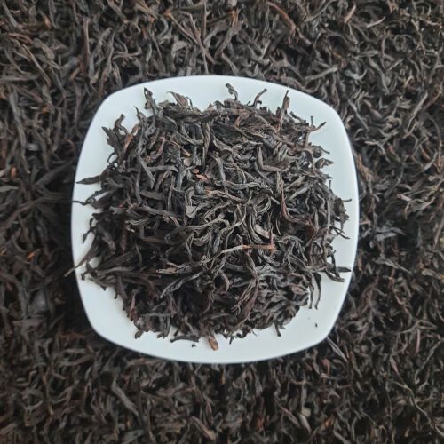 White square bowl filled with dark loose tea leaves on a bed of loose tea leaves