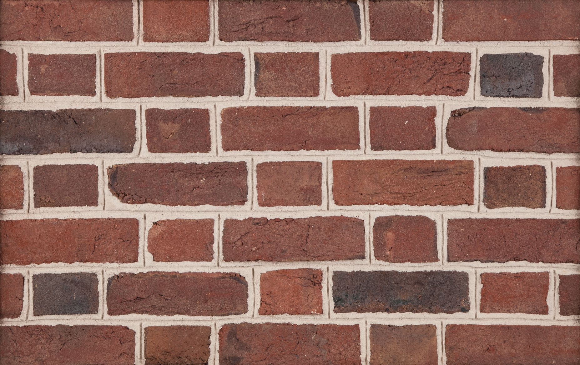 Brick wall with red and dark brown bricks, white mortar.