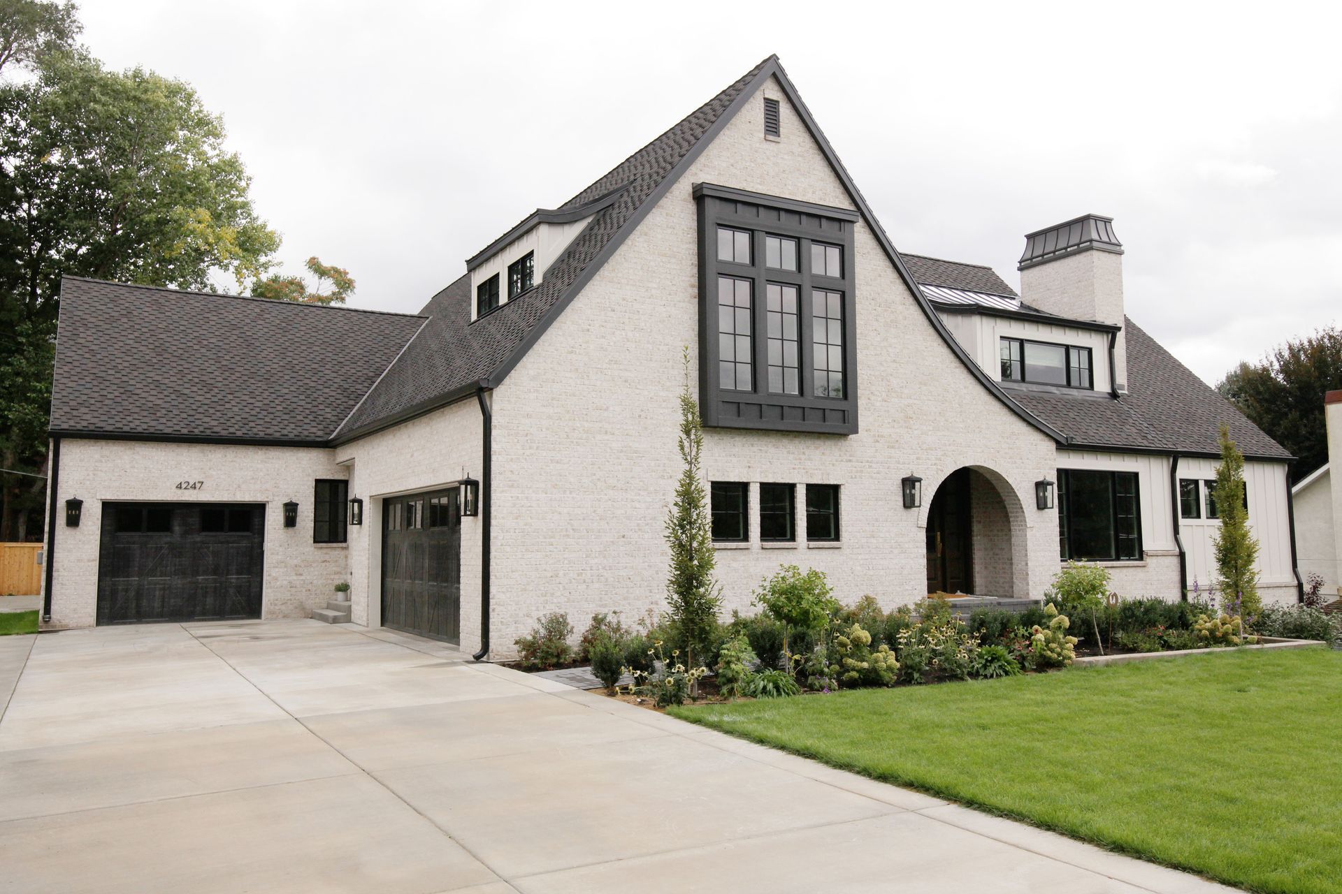 White brick house with black roof and trim, arched entry, and garage doors.