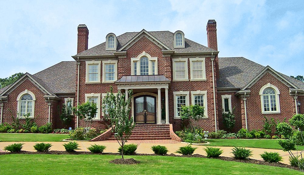 Red brick mansion with green lawn and blue sky.
