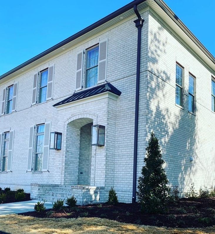 White brick house with shutters and a covered entryway. Sunny day.