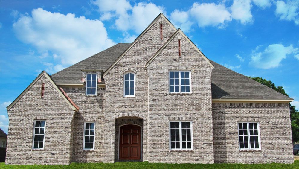 Two-story gray brick house with brown door, multiple windows, and a blue sky background.