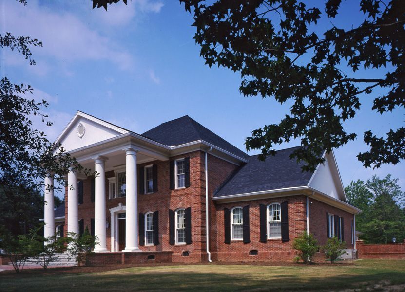 Two-story brick house with white columns and a black roof on a sunny day.