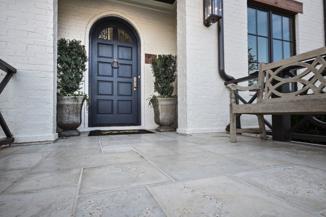 Stone patio leading to a dark blue front door with potted plants on either side and a wooden bench.