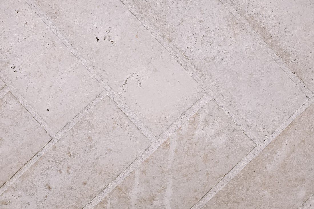 Herringbone pattern of pale, textured, rectangular pavers.