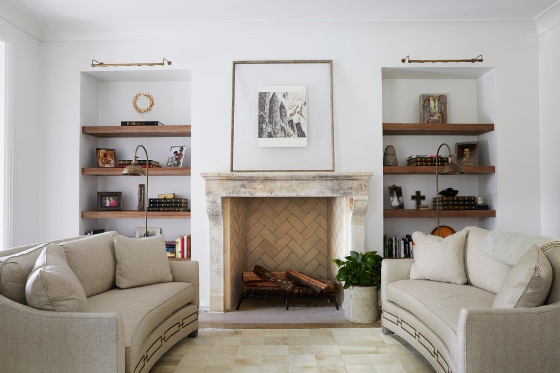 Living room with fireplace, built-in shelves, and two curved sofas. Neutral color palette with wooden elements.