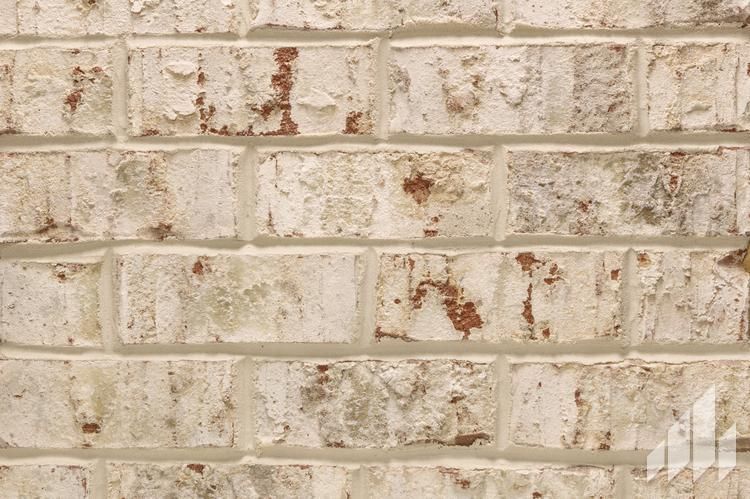 Close-up of a weathered brick wall with off-white and brown bricks, gray mortar.