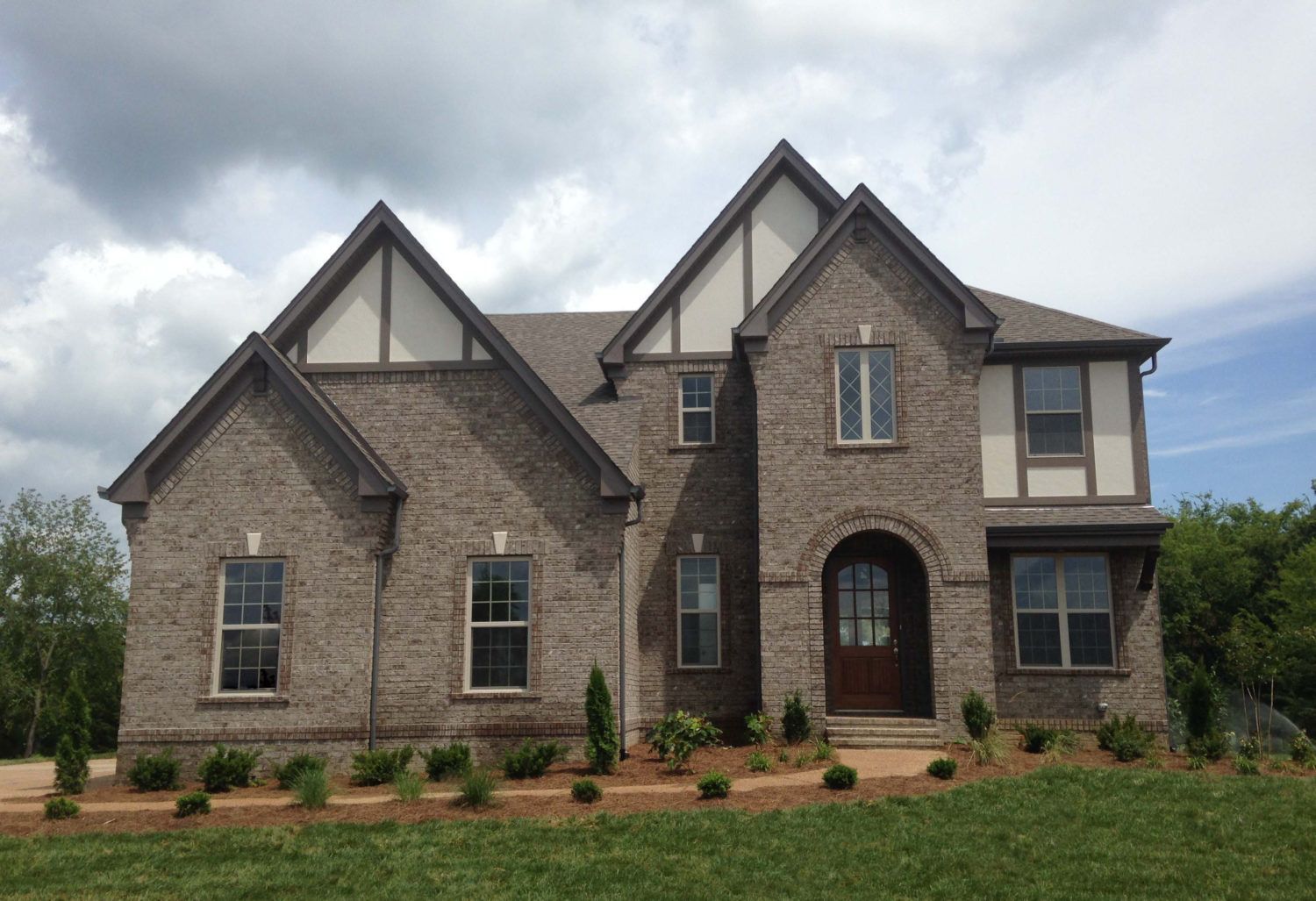 Two-story brick house with white trim, arched entryway, multiple windows, and a grassy lawn.